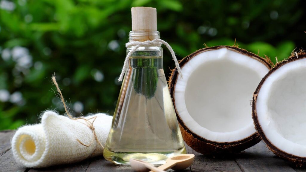 Olio MCT in boccetta di vetro con affianco due mezze noci di cocco e un telo arrotolato