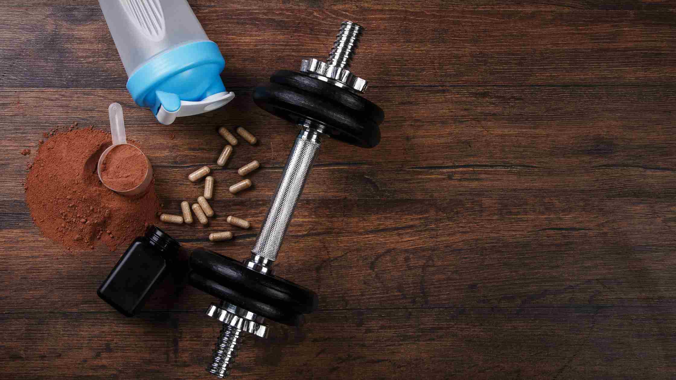 Alcune capsule di aminoacidi ramificati, un manubrio da palestra e una borraccia sopra un pavimento di legno