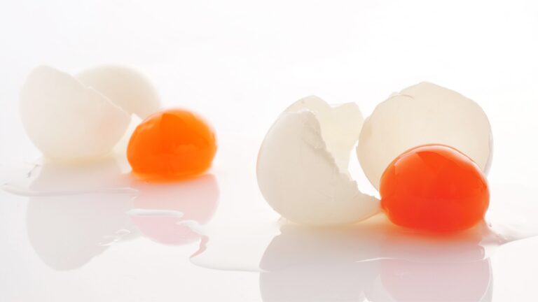 Due uova con il guscio rotto: fuoriescono i tuorli arancioni fonti di vitamina K2