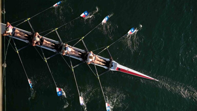 Foto dall’alto di quattro persone in una canoa a remi durante una gara di canottaggio, esempio di sforzo intenso che utilizza la glicolisi anaerobica