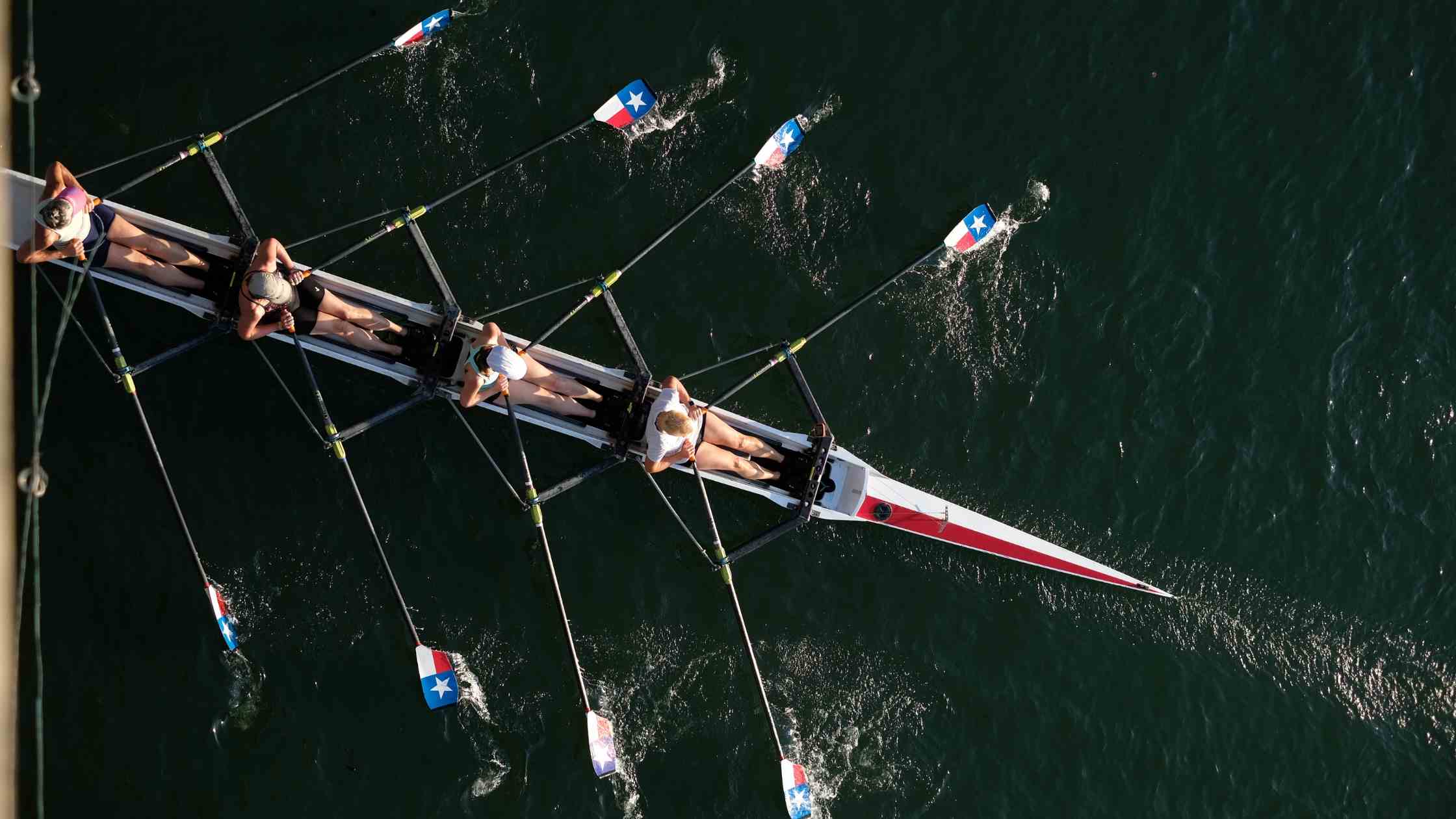 Foto dall’alto di quattro persone in una canoa a remi durante una gara di canottaggio, esempio di sforzo intenso che utilizza la glicolisi anaerobica