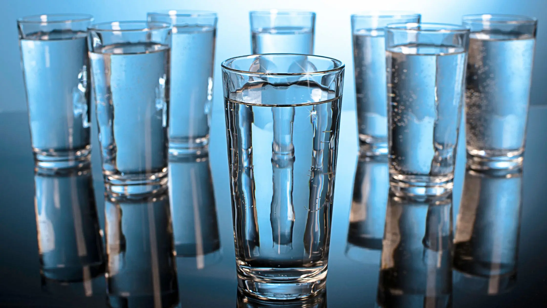 otto bicchieri d'acqua su un tavolo - il consumo minimo giornaliero per favorire l'idratazione