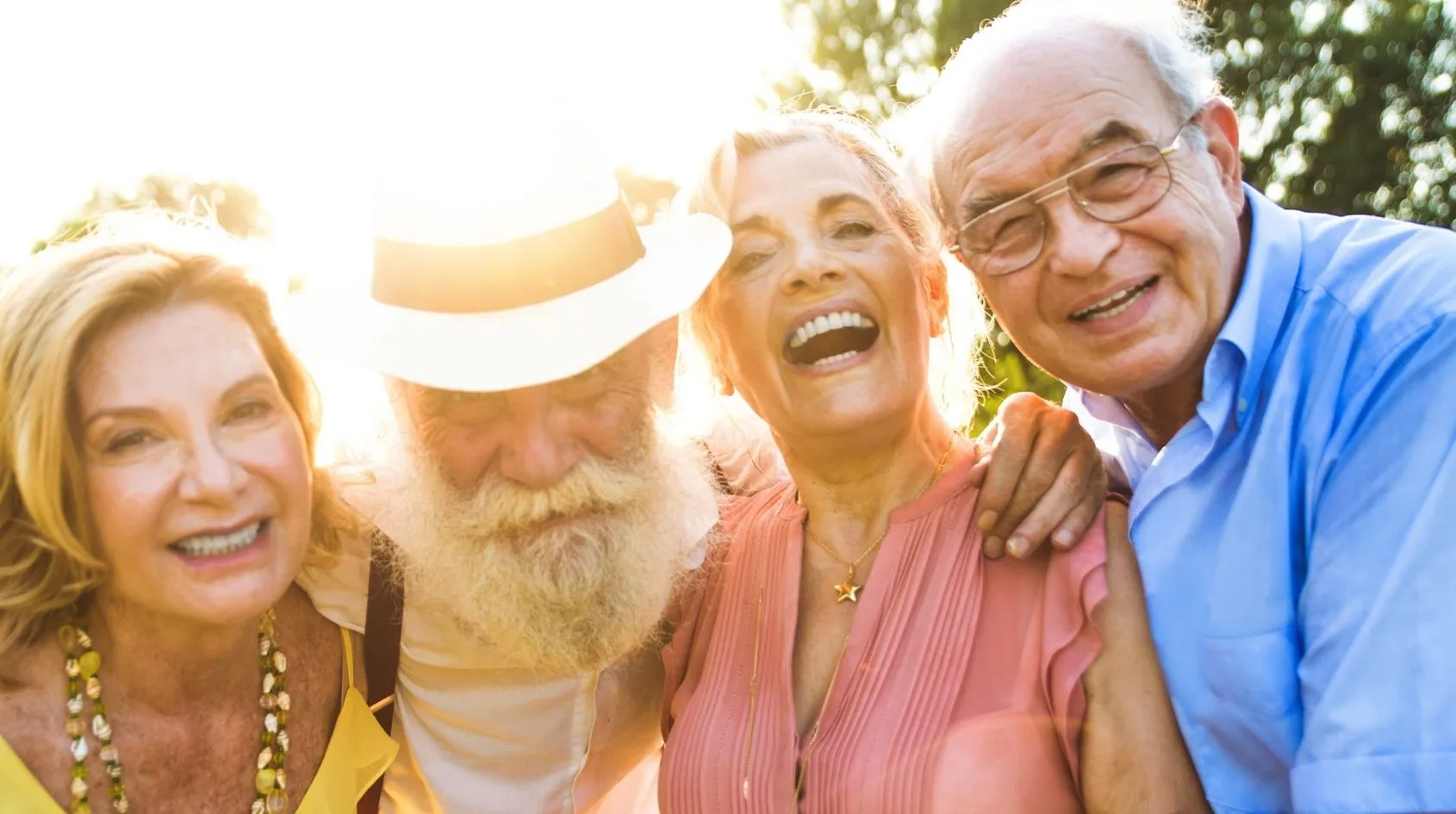 Gruppo di persone mature sorridenti all’aperto con luce solare, simbolo di salute e prevenzione.
