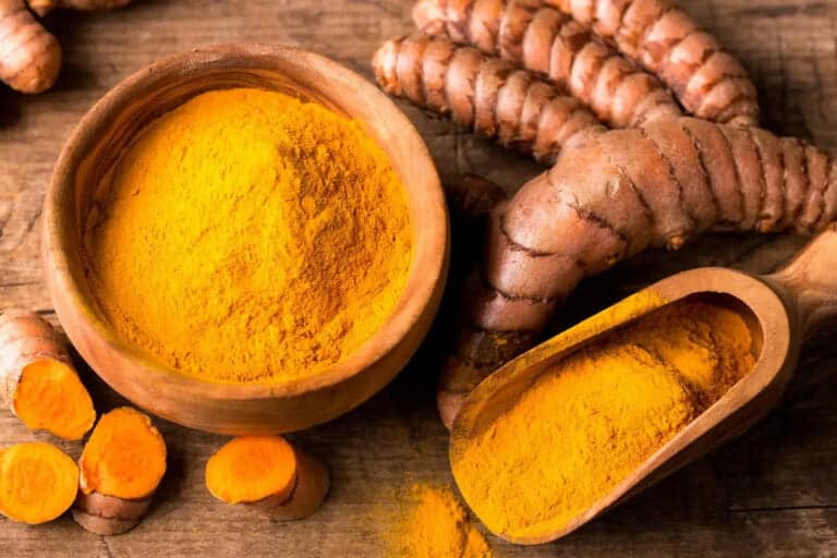 Polvere di curcuma in ciotola e radici fresche tagliate